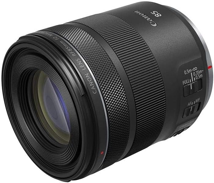 A Canon RF 85mm f/2 Macro IS STM lens displayed at an angle, showcasing its black exterior, focus and zoom controls, and the lens element through the glass.
