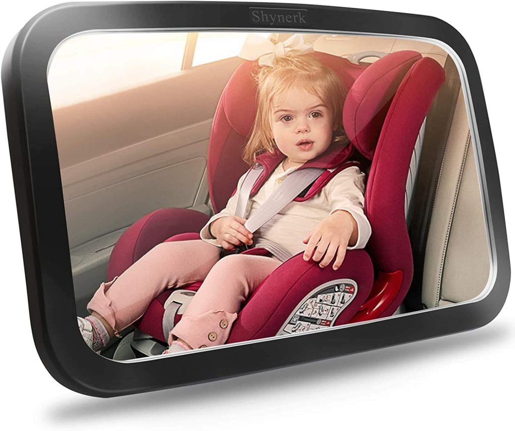 A young child securely strapped in a red car seat, looking at the camera. The scene highlights a backseat baby monitor in a vehicle.