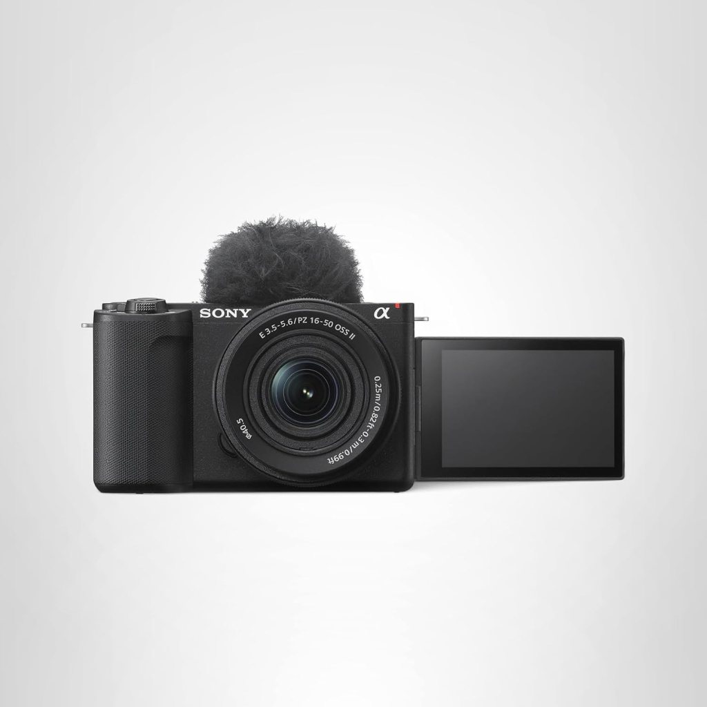 Front view of a Sony mirrorless camera with a 16-50mm lens and a fluffy microphone attached, with the screen flipped out.