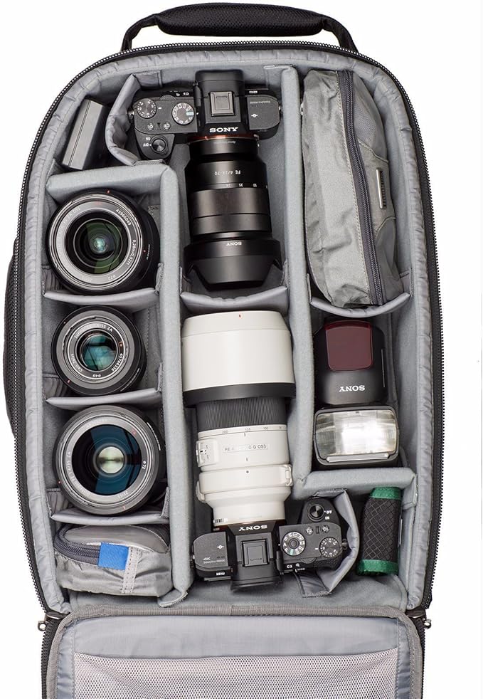 A camera bag interior featuring a Sony camera body, lenses of various sizes, a flash, and additional gear neatly organized in padded compartments.