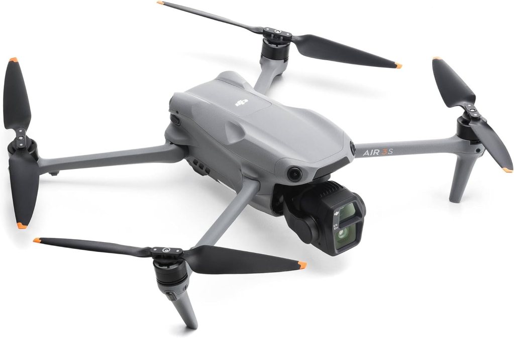 A grey drone with four black propellers and a camera mounted on the front, positioned on a white background.