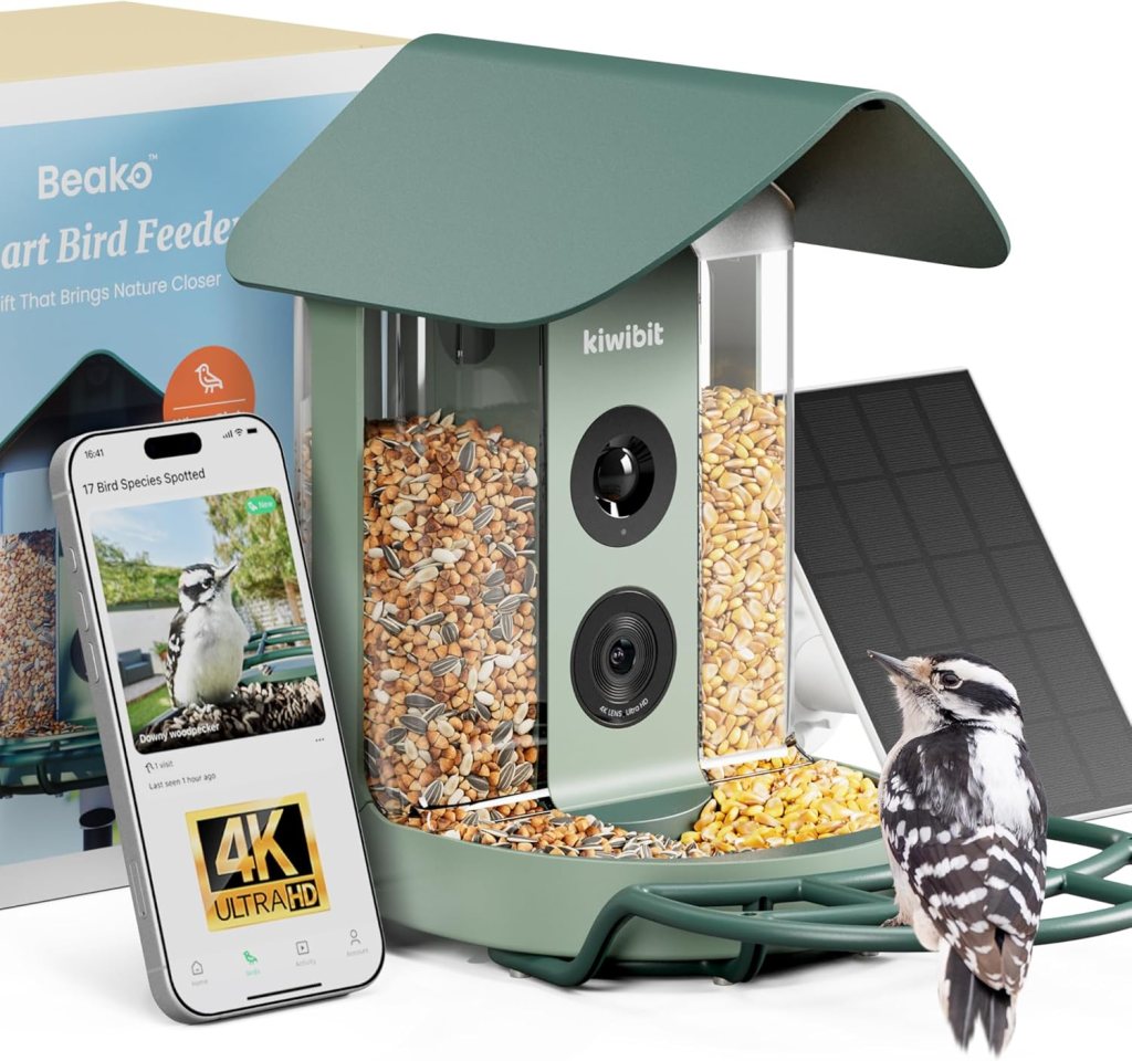 A smart bird feeder with a green lid, clear container filled with bird seeds, and a smartphone displaying a bird identification app. A woodpecker is perched beside the feeder.