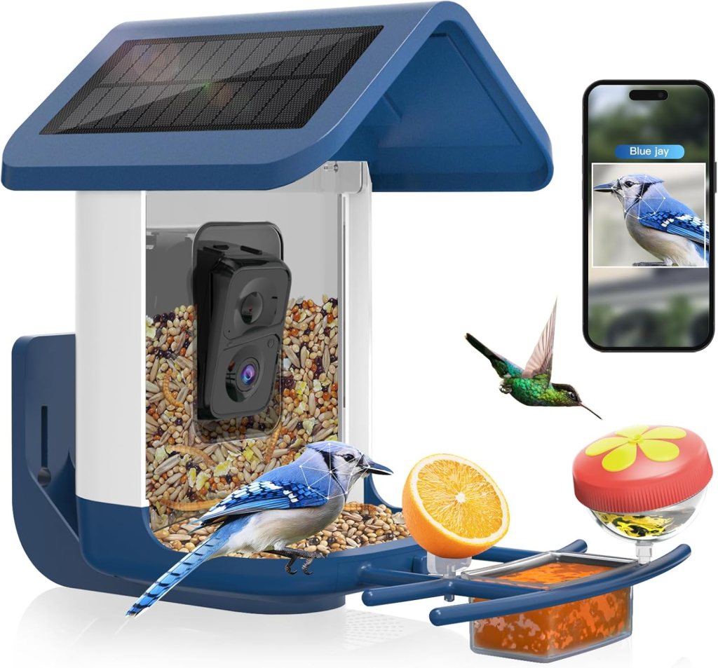 A modern bird feeder with a solar panel on the roof, filled with birdseed, featuring a built-in camera. Surrounding the feeder are images of a blue jay, a hummingbird, an orange slice, and a jelly dish, along with a smartphone displaying a blue jay profile.