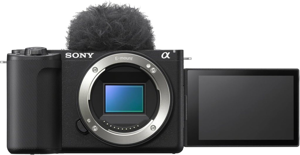 A Sony mirrorless camera with an E-mount, featuring a fur windscreen on the microphone and a flip-out LCD screen.