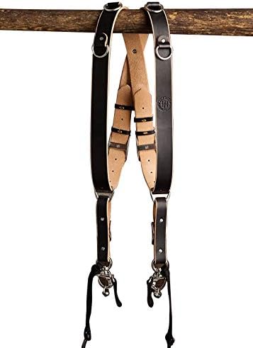 A pair of leather suspenders hanging from a wooden rail, featuring a combination of brown leather straps and lighter leather backing with adjustable buckles.