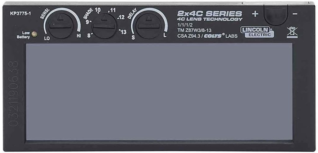 Close-up of a welding helmet display with adjustable settings for sensitivity, shade, and delay. Features include a low battery indicator.