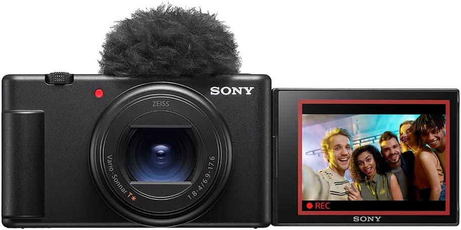 A Sony camera with a fuzzy microphone cover and a flipped-out screen displaying a group of smiling people taking a selfie.