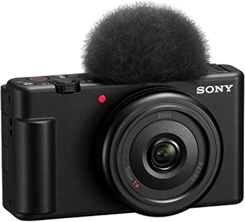 A Sony camera with a fuzzy windscreen mounted on top, featuring a Zeiss lens and recording buttons