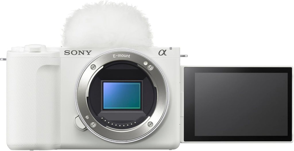 A white Sony mirrorless camera with an E-mount lens and a flip-out screen.