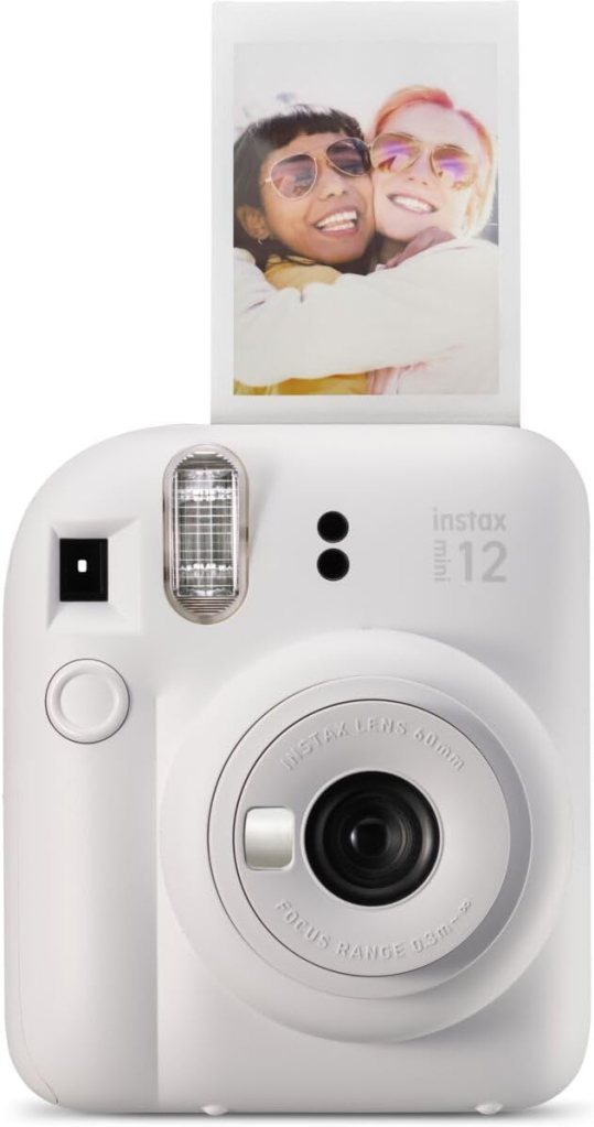 A white Instax Mini 12 instant camera, displaying a recent photo of two smiling friends embracing, wearing sunglasses.
